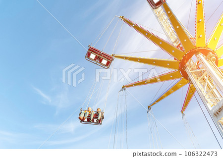 Scenic bottom view high chain swing flying carousel against blue sky. Merry go round roundabout chairoplane at portable amusement park. People enjoy having family fun play riding at fair festival Scenic bottom view high chain swing flying carousel against blue sky. Merry go round roundabout chairoplane at portable amusement park. People enjoy having family fun play riding at fair festival 106322473