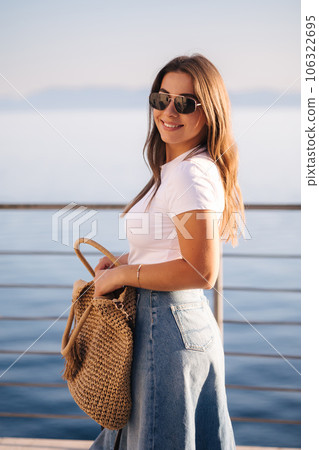 Portrait of gorgeous woman in sunglasses in front of sea. Attractive female in denim style stand on balcony in sunset time Portrait of gorgeous woman in sunglasses in front of sea. Attractive female in denim style stand on balcony in sunset time 106322695