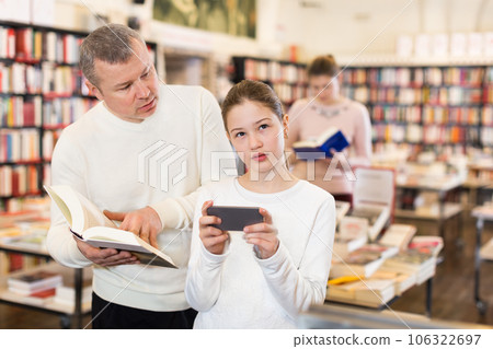 Preteen girl absorbed in phone in bookstore 106322697