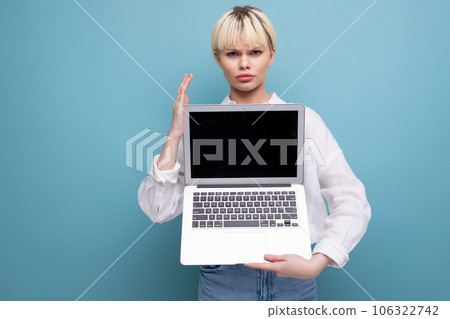 young blond caucasian woman with a short haircut dressed in a white shirt and jeans holds a laptop 106322742