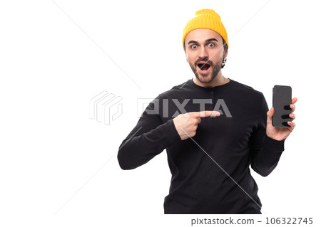 young surprised handsome caucasian brunette man with beard in informal style holding phone with 106322745
