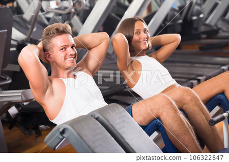 man and woman making sit ups together using machine in gym 106322847
