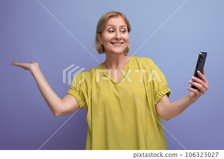 cheerful blond middle-aged woman joyfully masters gadget including smartphone cheerful blond middle-aged woman joyfully masters gadget including smartphone 106323027