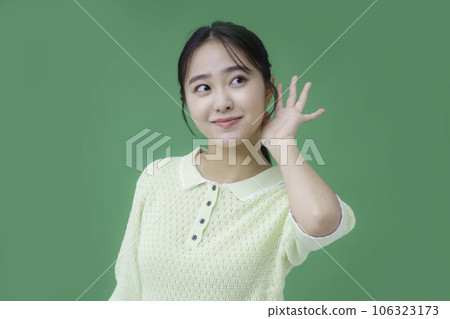 A young woman who puts her hands on her ears on a green background 106323173