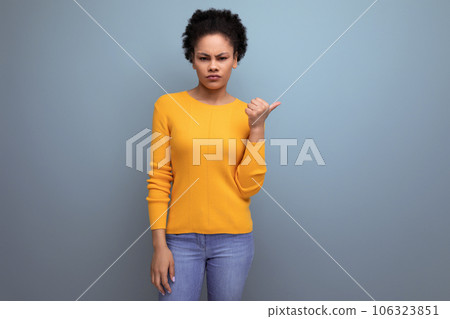 smart young latin woman with afro hair pointing finger to the side on gray background with copy 106323851