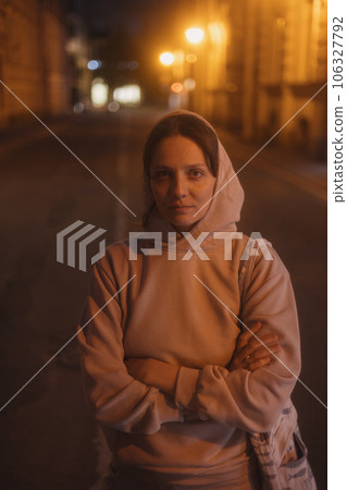 young thoughtful woman stands on road in beige hoodie. walk in evening in light of lanterns, young thoughtful woman stands on road in beige hoodie. walk in evening in light of lanterns, 106327792