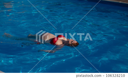 Pregnant woman floating in pool in red bikini.  106328210
