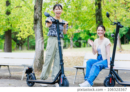 Female college student riding an electric kickboard with friends Female college student riding an electric kickboard with friends 106328367