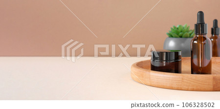 Glass bottles on wooden plate. Natural skin care SPA beauty product design. Mineral organic oil cosmetics on beige background. Earth tones. Mock-Up. Oily pipette. Face and body treatment. Front View 106328502