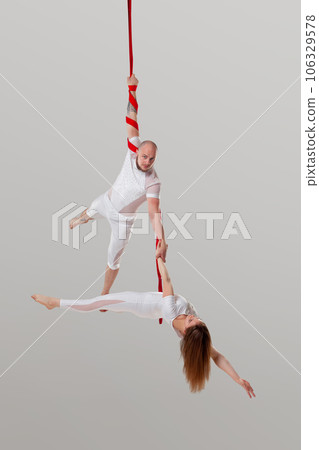 Beautiful girl and an athletic man in a white sport suits are performing an acrobatic elements in a studio. 106329578
