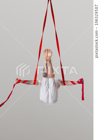 Athletic man in a white sport suit is performing an acrobatic elements in a studio. 106329587