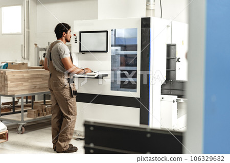 Young carpenter operating machine for wood processing at a furniture factory 106329682