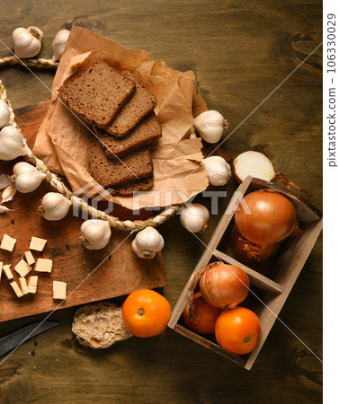 still life of food in a rural style on a dark wood background, rye bread and garlic, cheese, tomatoes and onion, concept of fresh vegetables and healthy food 106330029