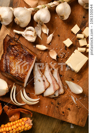 still life of food in a rural style on a dark wood background, sliced lard and garlic, cheese, corn and onion, concept of fresh vegetables and healthy food 106330044