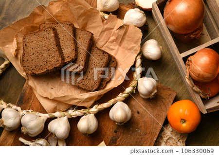 still life of food in a rural style on a dark wood background, rye bread and garlic, tomatoes and onion, concept of fresh vegetables and healthy food 106330069