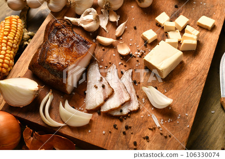 still life of food in a rural style on a dark wood background, sliced lard and garlic, cheese, corn and onion, concept of fresh vegetables and healthy food 106330074