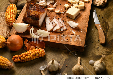 still life of food in a rural style on a dark wood background, sliced lard and garlic, cheese, corn and onion, concept of fresh vegetables and healthy food still life of food in a rural style on a dark wood background, sliced lard and garlic, cheese, corn and onion, concept of fresh vegetables and healthy food 106330080