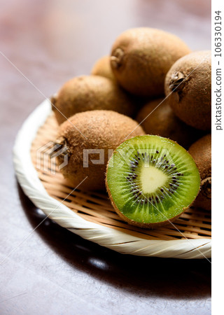 Kiwi fruit piled high in a colander on top of a jute bag and kiwi sliced into rings with visible cross-sections Kiwi fruit piled high in a colander on top of a jute bag and kiwi sliced into rings with visible cross-sections 106330194