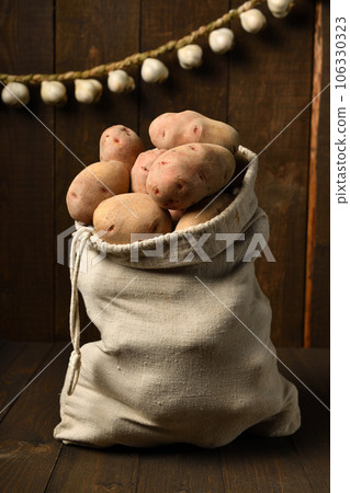 a bag full of potatoes and garlic bulbs, braided like a garland against a dark wood background a bag full of potatoes and garlic bulbs, braided like a garland against a dark wood background 106330323