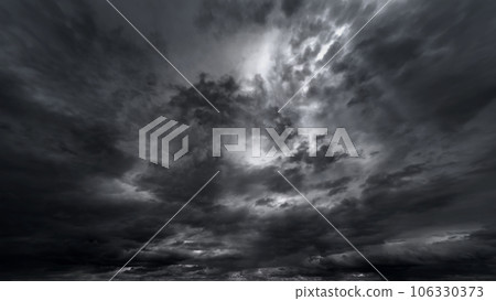 dark dramatic sky with black stormy clouds before rain or snow as abstract background, extreme weather, the sun shines through the clouds, high contrast photo 106330373