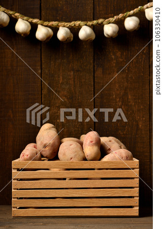 a wooden box full of potatoes and bunch of garlic on a dark wooden background, a wooden box full of potatoes and bunch of garlic on a dark wooden background, 106330410