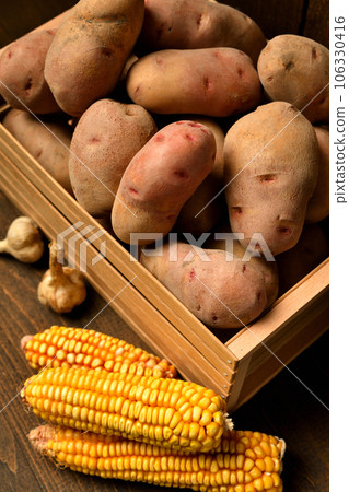 wooden box full of potatoes, garlic bulbs and corn cobs on dark wooden background 106330416