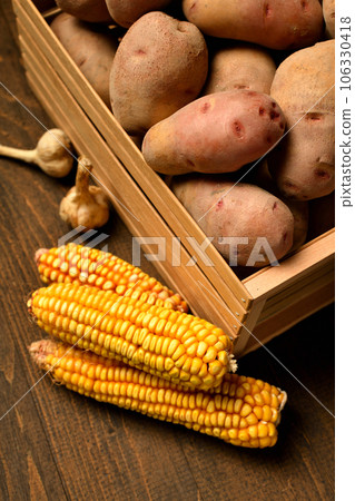 wooden box full of potatoes, garlic bulbs and corn cobs on dark wooden background 106330418