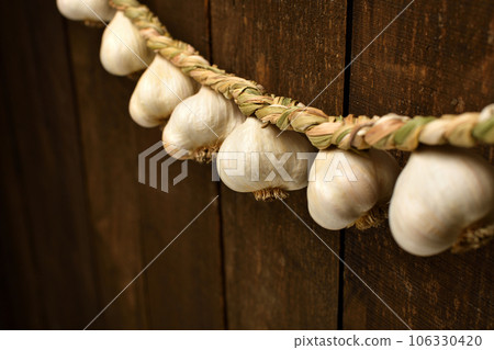 garlic bulbs braided in a pigtail like a garland on a background of dark wooden boards, an empty place for text 106330420