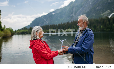 Portrait of senior couple holding a model of wind turbine, standing in the middle stunning nature. Portrait of senior couple holding a model of wind turbine, standing in the middle stunning nature. 106330846