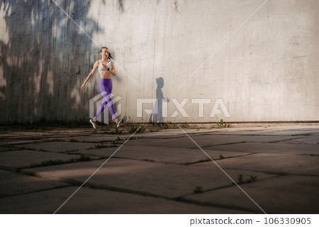 Fitness woman running in front of concrete wall casting shadow. 106330905