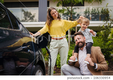 Happy family standing beside their car and charging electric car on the street. 106330954