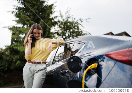 Close up of beautiful woman calling while charging her electric car on the street. 106330958
