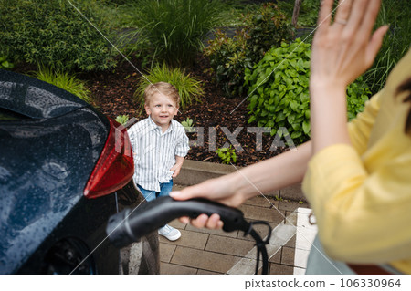 Cute little boy looking at his mother, while she charging electric car. 106330964