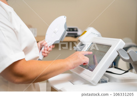 Beautician tries to adjust screen settings of laser hair removal machine in private clinic. Dermatologist waits for client to make appointment for laser hair removal Beautician tries to adjust screen settings of laser hair removal machine in private clinic. Dermatologist waits for client to make appointment for laser hair removal 106331205