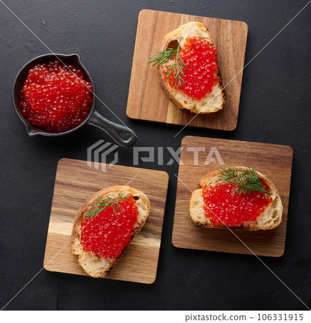 Red caviar on slices of white wheat bread on a black table, concept of luxury and gourmet cuisine, top view Red caviar on slices of white wheat bread on a black table, concept of luxury and gourmet cuisine, top view 106331915