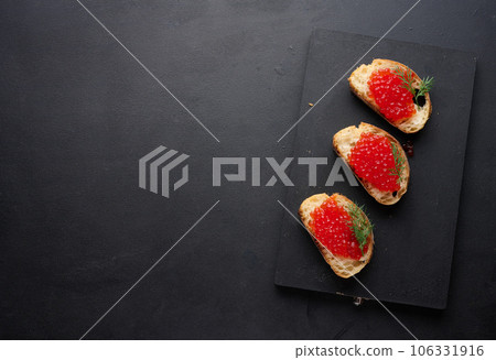 Red caviar on slices of white wheat bread on a black table, concept of luxury and gourmet cuisine, top view 106331916