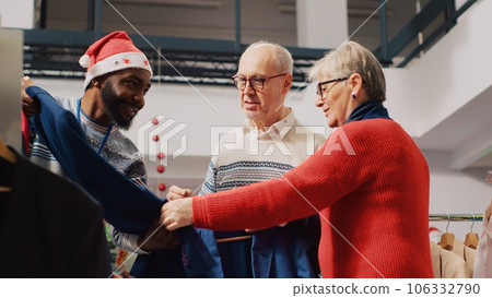 Retail assistant in xmas adorn fashion boutique helping old couple during their Christmas frenzy shopping spree. Worker offering advice to aged clients during festive holiday season 106332790