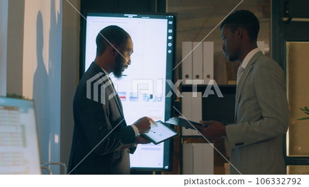 African american company stakeholders discussing quarterly profit revenue, analyzing financial stats in front of digital screen. Businessmen looking at key data graphs in office 106332792