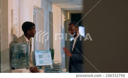 Happy coworkers discussing holiday plans during nightshift break in office. Smiling employee enjoying downtime at work, drinking cup of coffee while chatting with friendly colleague 106332798