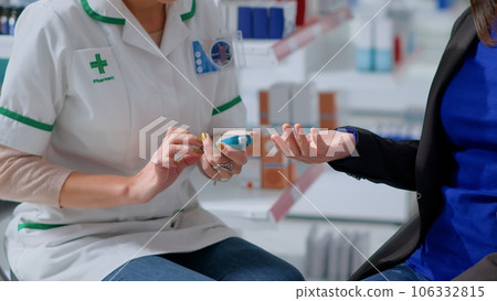 Close up of pharmacist in chemist store using medical diabetes examination tool to check patient glucose levels in blood. Expert and client in annual exam, doing checkup to preventing hypoglycemia 106332815