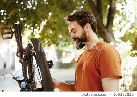 Active determined male cyclist confidently repairing bike rim and inspecting tire for outdoor leisure cycling. Dedicated sports-loving man performing bike maintenance essential work tool. 106332826