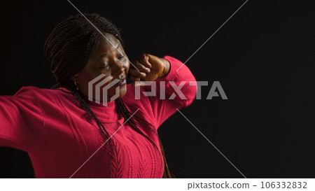 Female fashion influencer in isolated black background yawning to show her fatigue after hard day. Side-view portrait of fashionable african american woman covering her mouth. Female fashion influencer in isolated black background yawning to show her fatigue after hard day. Side-view portrait of fashionable african american woman covering her mouth. 106332832