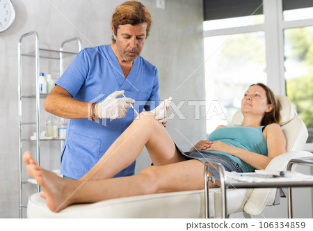 Experienced cosmetologist doing knee contouring injections to woman 106334859