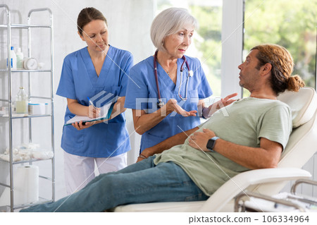 Man sitting in chair and carefully answers mature female doctor questions about well-being Man sitting in chair and carefully answers mature female doctor questions about well-being 106334964