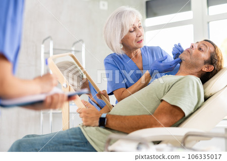 Male patient sitting on examination couch with mirror during consultation of cosmetologist Male patient sitting on examination couch with mirror during consultation of cosmetologist 106335017
