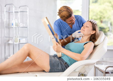 Male beautician giving consultation to woman patient with mirror in aesthetic clinic Male beautician giving consultation to woman patient with mirror in aesthetic clinic 106335049
