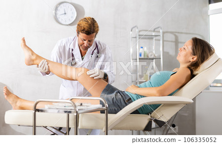 Adult male doctor examining leg of female patient Adult male doctor examining leg of female patient 106335052