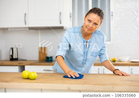 Positive female using a rag for cleaning tabletop at cozy apartment Positive female using a rag for cleaning tabletop at cozy apartment 106335060
