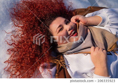 Top view of a fat red-haired woman lying on the snow. 106335923