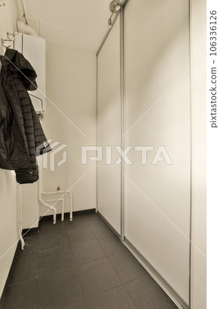 a coat hanging on a wall in a room with white walls and black tile flooring, there is an open door to the 106336126